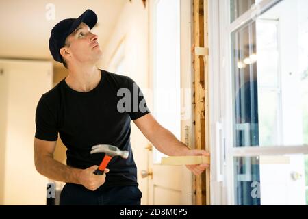 Un bel giovane uomo che installa la doppia porta scorrevole del patio dentro un nuovo cantiere Foto Stock