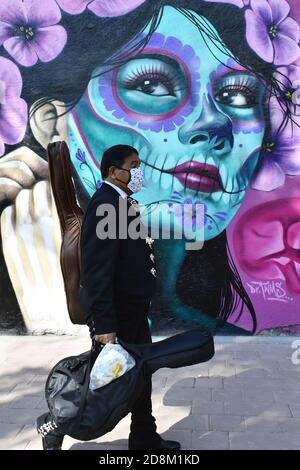 Città del Messico, Messico. 30 Ott 2020. CITTÀ DEL MESSICO, MESSICO - 30 OTTOBRE: Un Mariachi cammina davanti a un graffito che rappresenta il giorno del Messico delle tradizioni morte per commemorare le vittime che hanno perso la vita a causa della malattia di Covid-19 il 30 ottobre 2020 a Città del Messico, Messico. Credit: Carlos Tischler/Eyepix Group/The Photo Access Credit: The Photo Access/Alamy Live News Foto Stock