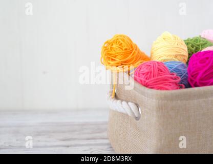 Fili colorati per la lavorazione a maglia in un cestello su un sfondo di legno Foto Stock