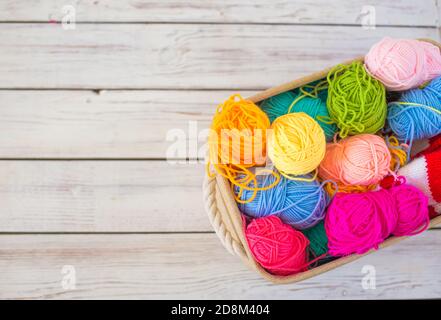 Fili colorati per la lavorazione a maglia in un cestello su un sfondo di legno Foto Stock