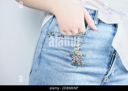 mano femminile che tiene un pendente di tartaruga gemma. mano della giovane donna in una tasca di jeans con tartaruga di gemma appesa. acsessories beautiful spakling. concetto di festa. Foto Stock