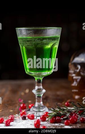 Cocktail verde sulla base di assenzio in un elegante vintage vetro su di un legno marrone. sfondo dello zucchero bianco e mirtilli sono sparsi nei dintorni Foto Stock