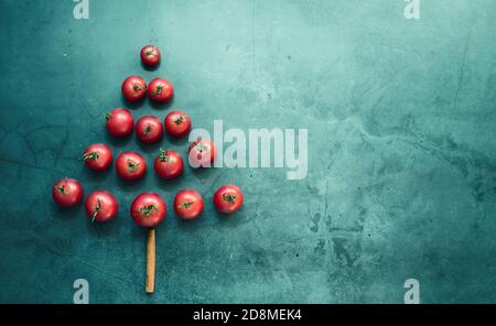 Layout creativo di rami di albero di Natale fatto di veri pomodori ciliegia su uno sfondo colorato. Concetto del nuovo anno della natura. Foto Stock