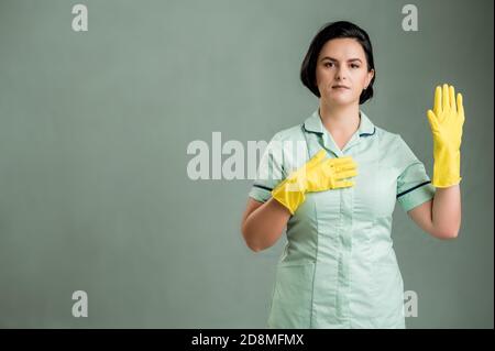 Giovane donna che indossa una camicia verde e guanti gialli, mostrando giuramento isolato su sfondo verde Foto Stock