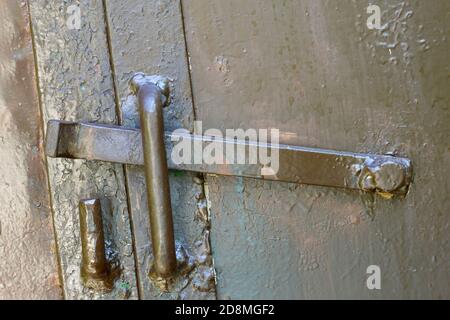 Primo piano di illuminato dal sole vecchio gancio di blocco in metallo grezzo su garage o cancello di ferro fienile. Tecnologia obsoleta, sicurezza, sicurezza e protezione dai ladri conce Foto Stock