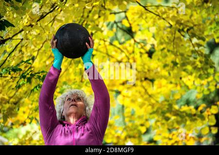 Una donna negli anni sessanta che solleva pesi all'aperto durante l'autunno. Foto Stock
