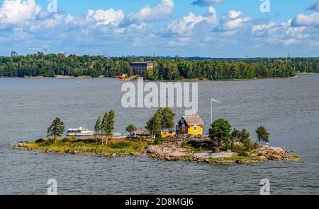 Piccola isola rocciosa con piccola casa di legno gialla e bandiera Della Finlandia Foto Stock