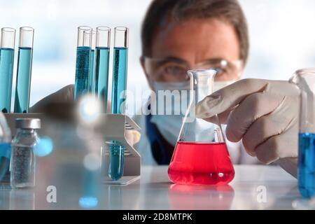 Dettaglio dello scienziato che guarda attentamente un liquido rosso in un pallone su un tavolo da laboratorio. Composizione orizzontale. Vista frontale. Foto Stock