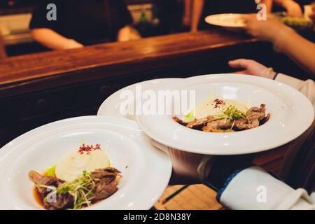 Il cameriere è in possesso di un piatto delizioso succosa carne cotolette, purè di patate cosparso di verdi e sane fresca insalata di pomodori e lattuga Foto Stock