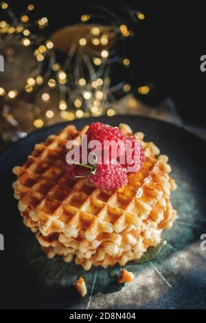 Waffle dorati dolci e freschi. Servite i deliziosi waffle viennesi con lamponi freschi maturi su un bel piatto con sfondo garland. Waffle su Foto Stock