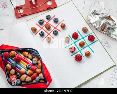 Pausa pranzo sana durante il concetto di lezione. Portamatite confezionato con bacche, noci, penne e matite e giochi di puzzle tic-tac-toe con bacche e noci Foto Stock