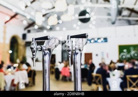 Doppio rubinetto della birra e bobina su un bar ristorante, con i commensali fuori fuoco in background. Foto Stock