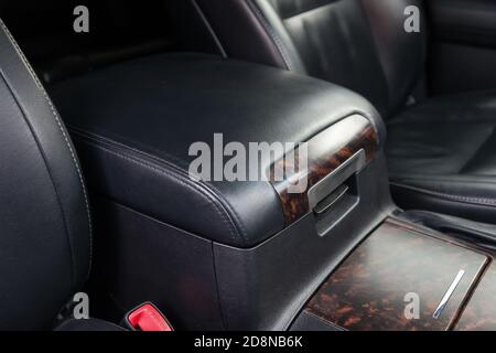 Primo piano del bracciolo tra i sedili anteriori all'interno dell'auto su un pannello in legno rivestito in pelle nera. Cassetto portaoggetti per riporre oggetti di piccole dimensioni Foto Stock