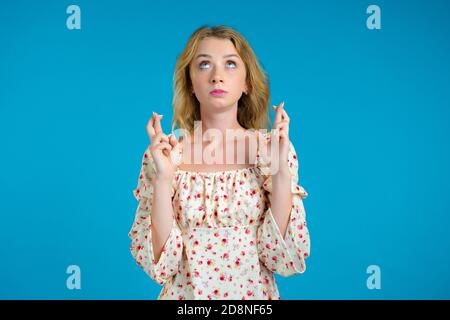 Bella ragazza che prega su sfondo blu. Donna che prega qualcuno soddisfare i suoi desideri, aiuto con. Foto Stock