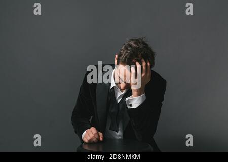 Studio ritratto di un giovane caucasico in un tuxedo, mano in capelli, tristemente guardando verso il basso, su uno sfondo studio semplice Foto Stock