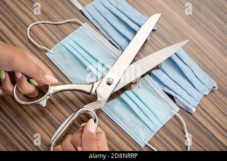 La mano di una donna poggia sulla scrivania, proprio accanto ad essa, grandi forbici da sarto e maschere protettive blu indossate. Foto Stock