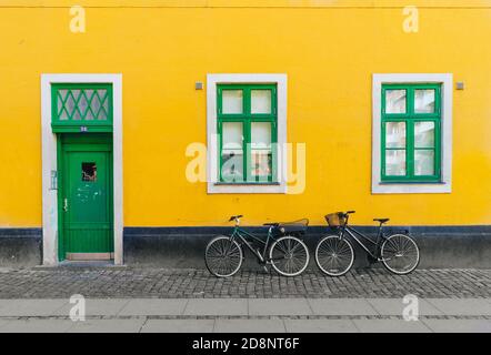 Copenhagen, Danimarca - 08/19/2017: Biciclette appese contro il muro giallo e porte e finestre di legno verde sulla strada Foto Stock