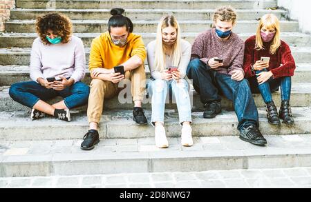 Amici multirazziali con maschere facciali che utilizzano smartphone Le scale nelle strade della città - giovani millenni a guardare contenuti sui medi sociali Foto Stock