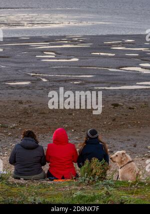 tre donne o amici con il cane seduti sulla costa della spiaggia al tramonto birdwatching a snettisham sulla costa nord del norfolk a bassa marea. Foto Stock