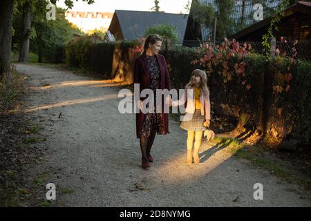 famiglia, stagione e concetto di gente - madre felice e bambina camminando lungo il parco autunnale vicino alla strada nel villaggio Foto Stock