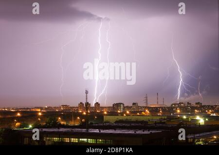 Il potente fulmine colpisce la città di notte. Un forte colpo di fulmine su un cielo grigio scuro colpisce la terra, illuminando la città Foto Stock