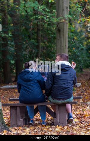 coppia seduta su una panchina che chiacchiera in un ambiente boschivo nella stagione autunnale Foto Stock