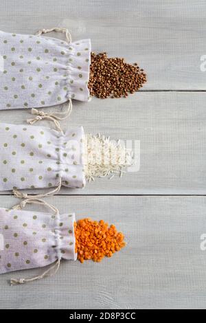 Tre tipi di cereali grezzi grano saraceno, riso e lenticchie in sacchi di tela su fondo bianco di legno. I grani sono sparsi sulla tabella. cerea sano organico Foto Stock