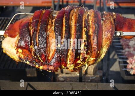 Un pezzo di maiale croccante su una spiedo di rotisserie in occasione di un barbecue. Un pezzo di carne grande su uno spiedo Foto Stock