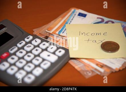Imposta sul reddito scritta su nota post-it con banconote, moneta e calcolatrice. Concetto: Pagamento dell'imposta sul reddito. Foto Stock