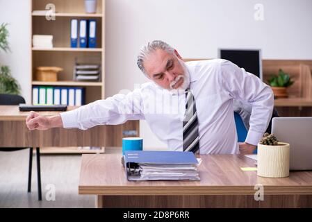 Anziano dipendente che soffre di radicolite sul posto di lavoro Foto Stock