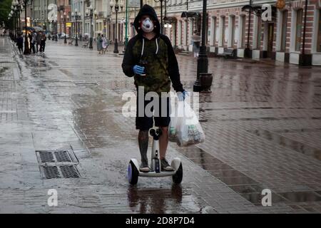 Mosca, Russia. 10 giugno 2020 UN giovane uomo che indossa la maschera porta il cibo su uno scooter elettrico autobilanciato da un negozio di alimentari in via Arbat nel centro di Mosca durante il romanzo coronavirus COVID-19 pandemia in Russia Foto Stock