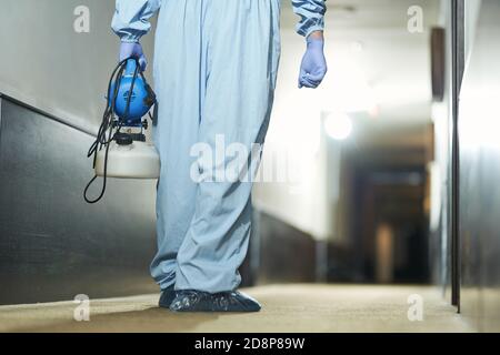 Vista posteriore dell'operatore sanitario con spray per rimuovere i batteri dalla superficie dell'hotel. Concetto di coronavirus e quarantena Foto Stock