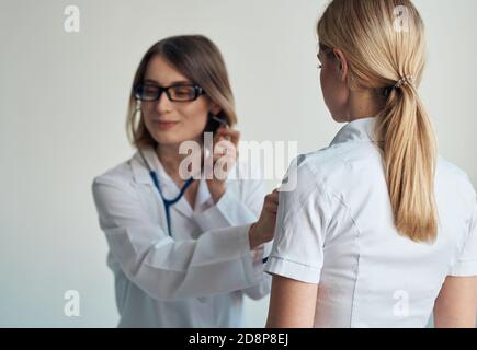 Il medico ascolta il battito cardiaco del paziente attraverso uno stetoscopio su uno sfondo chiaro vista ritagliata Foto Stock