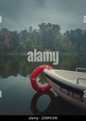 Moody sfondo autunno con una barca sulle acque calme del lago con un vibrante anello rosso di vita. Alberi cadenti colorati che si riflettono sulla superficie dello stagno in un c Foto Stock