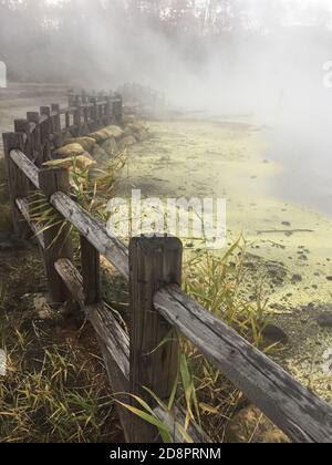 Una recinzione di legno circonda una sorgente calda fumante circondata da zolfo giallo Foto Stock