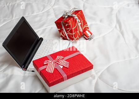 Concetto di shopping online. Scatole regalo rosse e computer portatile con schermo vuoto su sfondo bianco Foto Stock