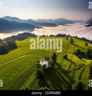 CERKEV Marijinega, Slovenia - veduta aerea della Chiesa di Maria (CERKEV Marijinega) in una soleggiata mattinata estiva con le alpi slovene sullo sfondo Foto Stock