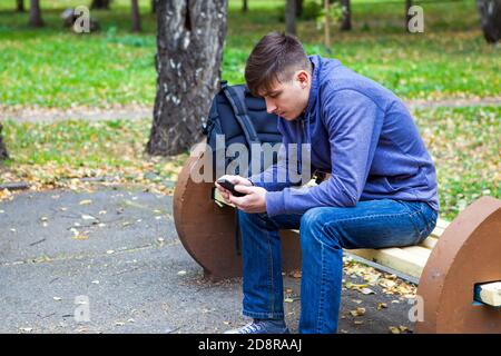 L'uomo giovane pensivo con un telefono siediti sul banco Nel Parco Autunno Foto Stock