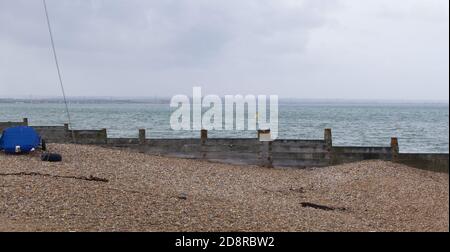 Breakwater sulla spiaggia di ghiaia con il mare verde grigio dietro con copyspace Foto Stock