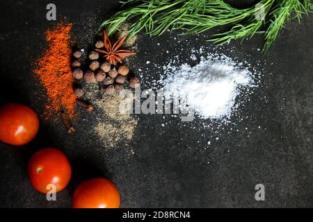 Diversi tipi di spezie, aneto, prezzemolo, pomodori ciliegini su fondo di pietra nera. Concetto di caffetteria. Consegna di cibo delizioso Foto Stock