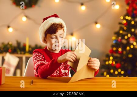 Ragazzino che mette la sua lettera e lista dei desideri in un Busta prima di inviarli a Babbo Natale Foto Stock