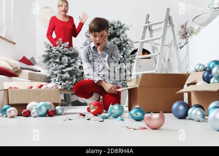 Buon Natale e buone feste! Mamma e figlio decorano l'albero di Natale all'interno. Accidentalmente il bambino rompe le palle, stupito guarda il Foto Stock