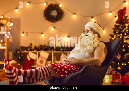 Santa stanco rilassarsi in comoda poltrona dopo una lunga giornata di lavoro e. Guardare lo spettacolo televisivo di Natale Foto Stock