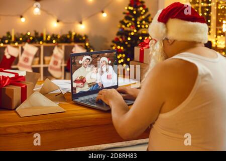 Nonno in camicia, cappello di Santa e barba videochiama la sua famiglia la vigilia di Natale Foto Stock