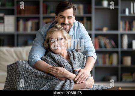 Ritratto di giovane uomo che copre sorridente madre in pensione in plaid. Foto Stock