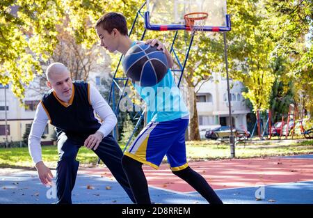 Fratelli che giocano a basket uno su uno. Fratello maggiore che insegna / istruendo il suo fratello più giovane il fratello migliore si muove nel gioco. Sport e stile di vita sano. Foto Stock