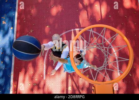 Fratelli che giocano a basket uno su uno. Sparare al cesto e guardare il volo della palla. Vista dall'alto sulla rete. Concetto di stile di vita sano. Foto Stock