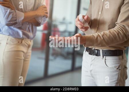 Disinfezione delle mani sul lavoro. Un'immagine ritagliata di un lavoratore di un ufficio maschile che utilizza uno spray igienizzante mentre si trova in piedi con un collega all'interno Foto Stock