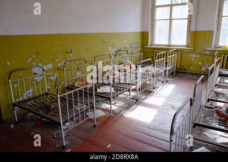 Letti per bambini in un asilo abbandonato. L'interno di un locale in uno degli edifici della zona di esclusione radioattiva di Chernobyl. Foto Stock