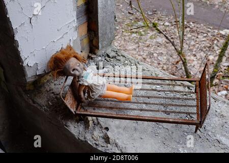 Bambola creepy su un lettino giocattolo. Giocattoli abbandonati in un asilo nido a Pripyat. Foto Stock